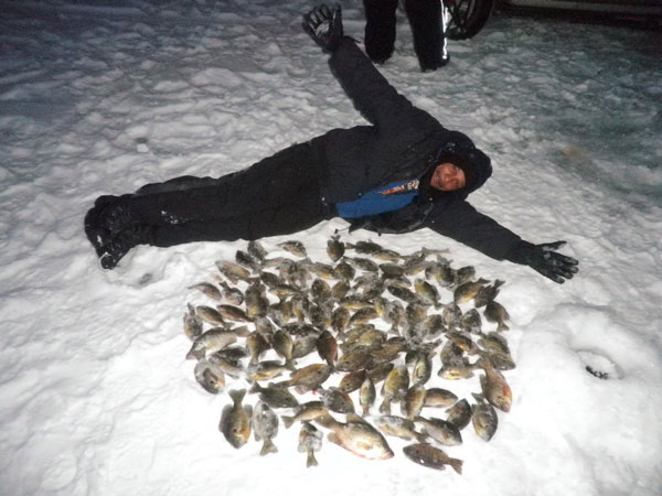 man on frozen lake laying next to a pile of fish he caught